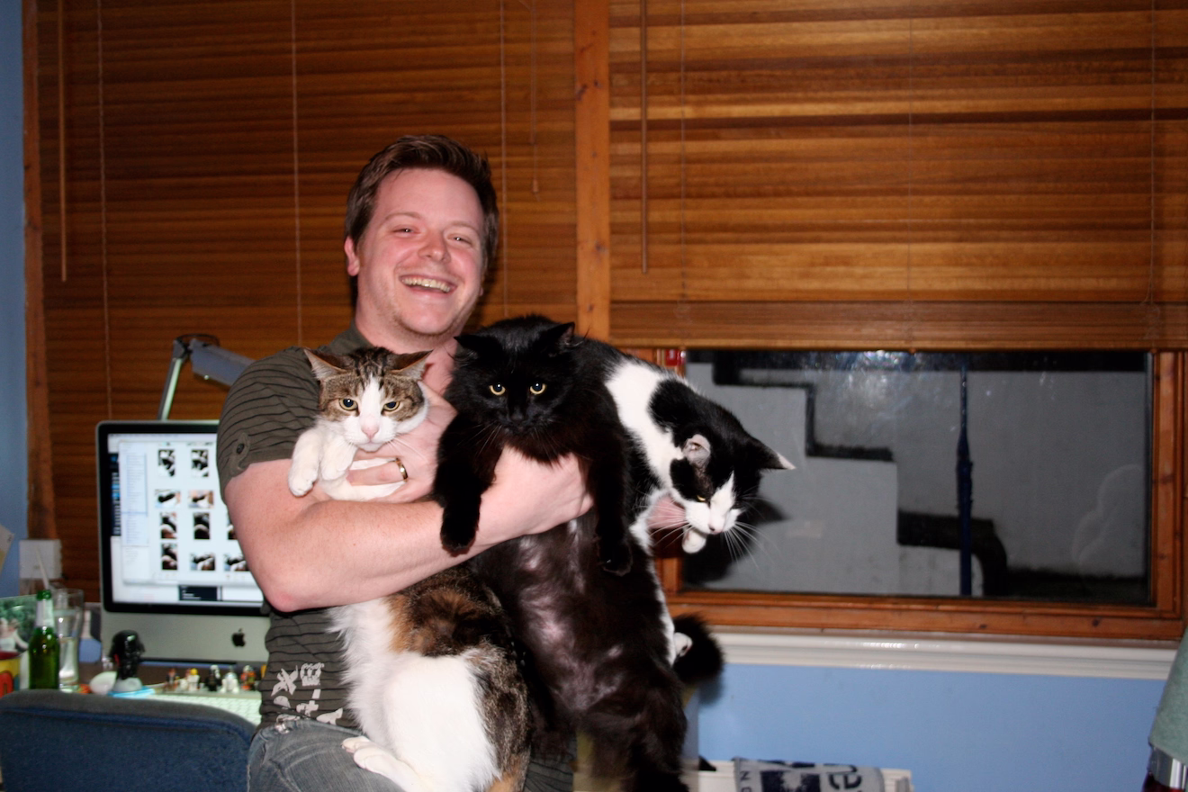 Remy awkwardly holding his three cats, one black and white, one tabby and one long haired